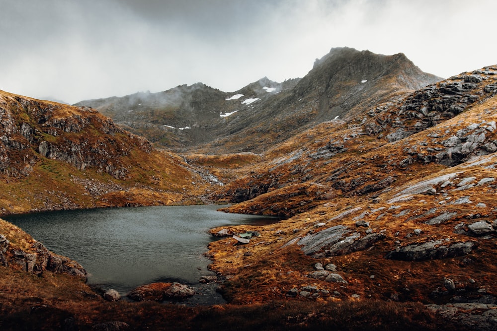 brown and green mountains beside river under white clouds during daytime