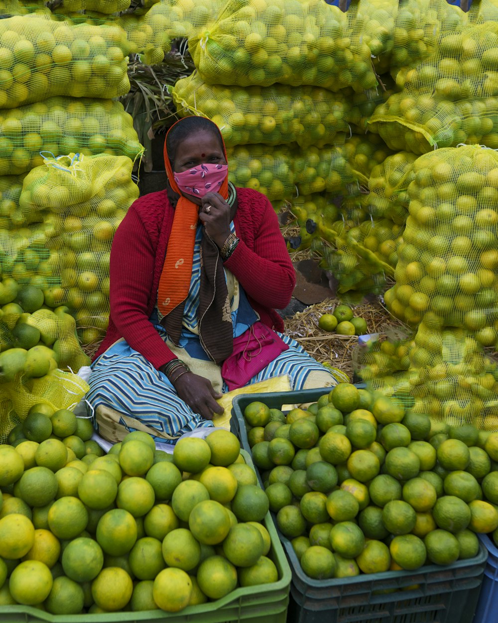 woman in red and black jacket sitting on green fruits