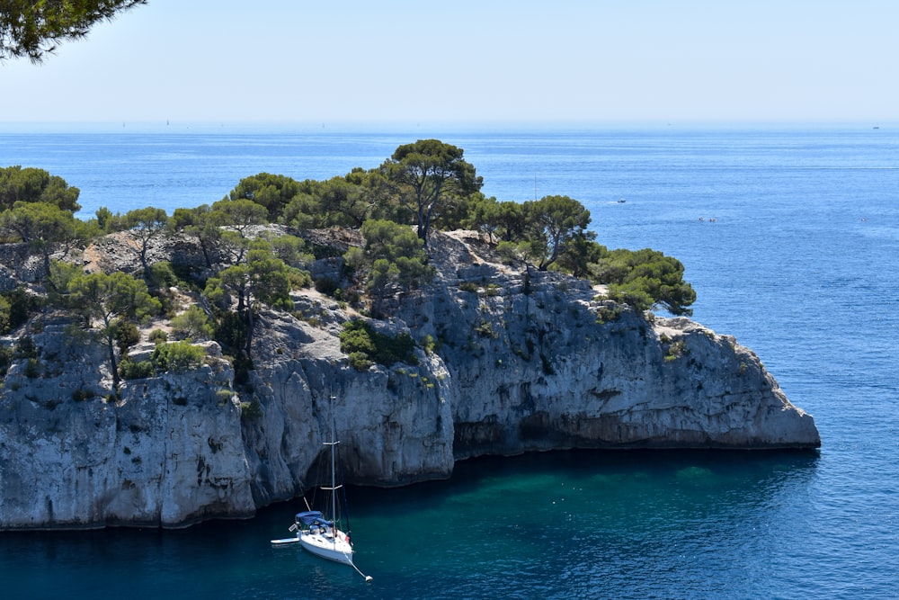 barca bianca sul mare vicino alla formazione rocciosa verde e marrone durante il giorno