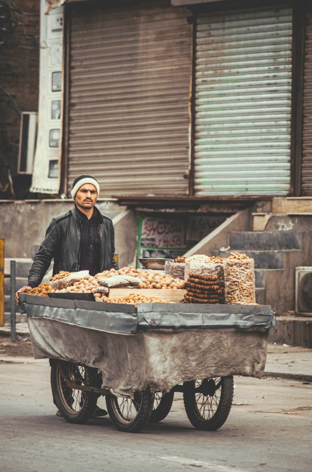 man in black jacket standing in front of brown and gray food cart