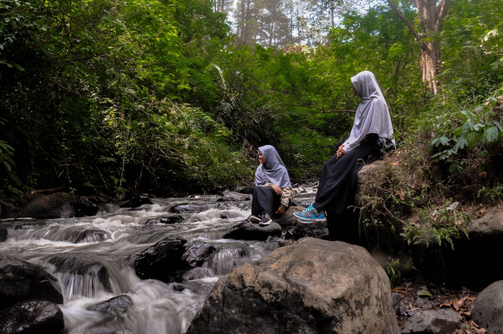 man in gray hoodie sitting on rock near river during daytime