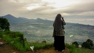 A traveler standing atop a lush green hill overlooking a misty valley.