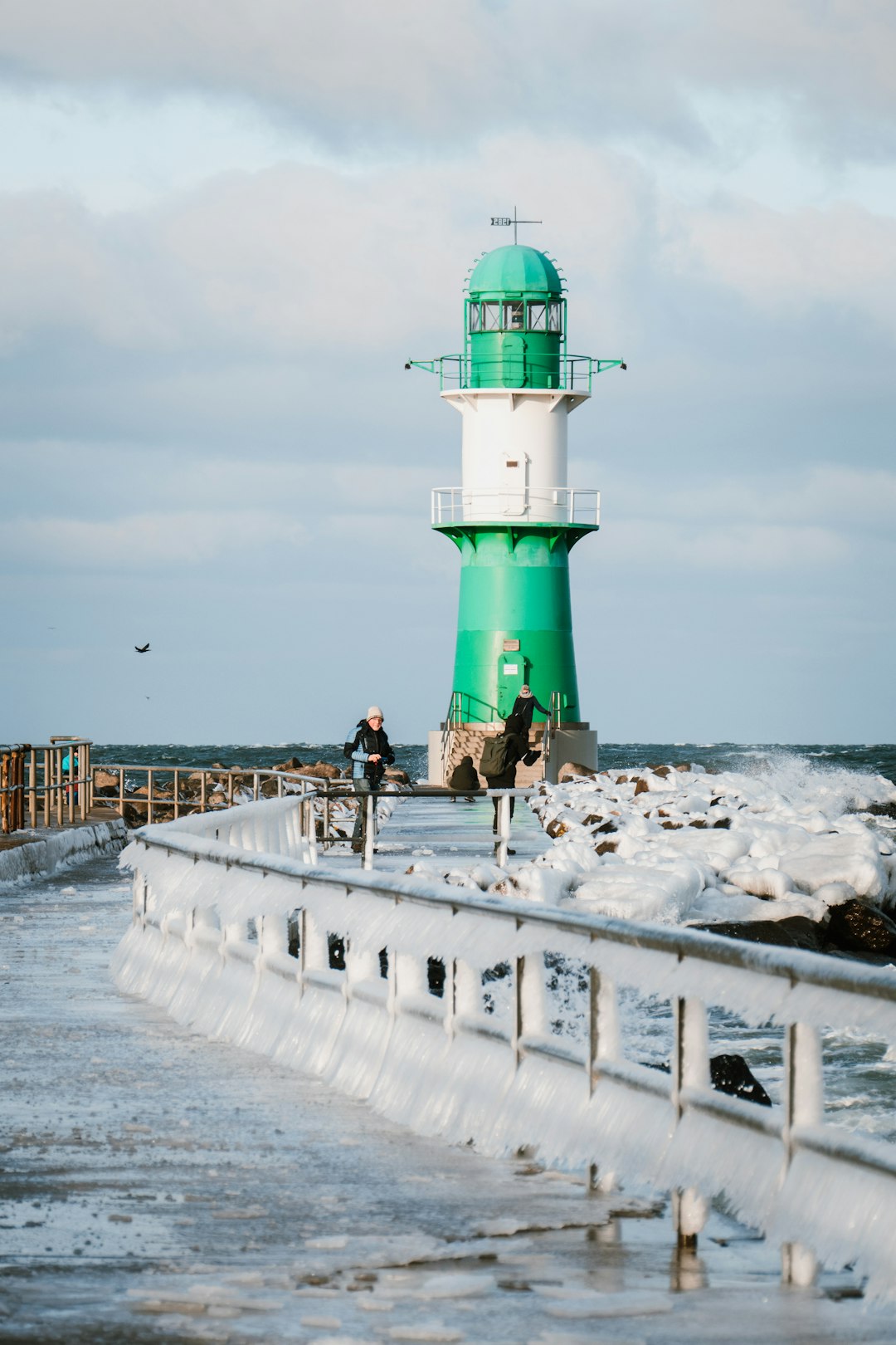 people walking on white snow covered dock near green and white lighthouse during daytime