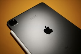 A sleek, modern tablet featuring a prominent logo, accompanied by a stylus. The device is set against a warm-toned, muted background.