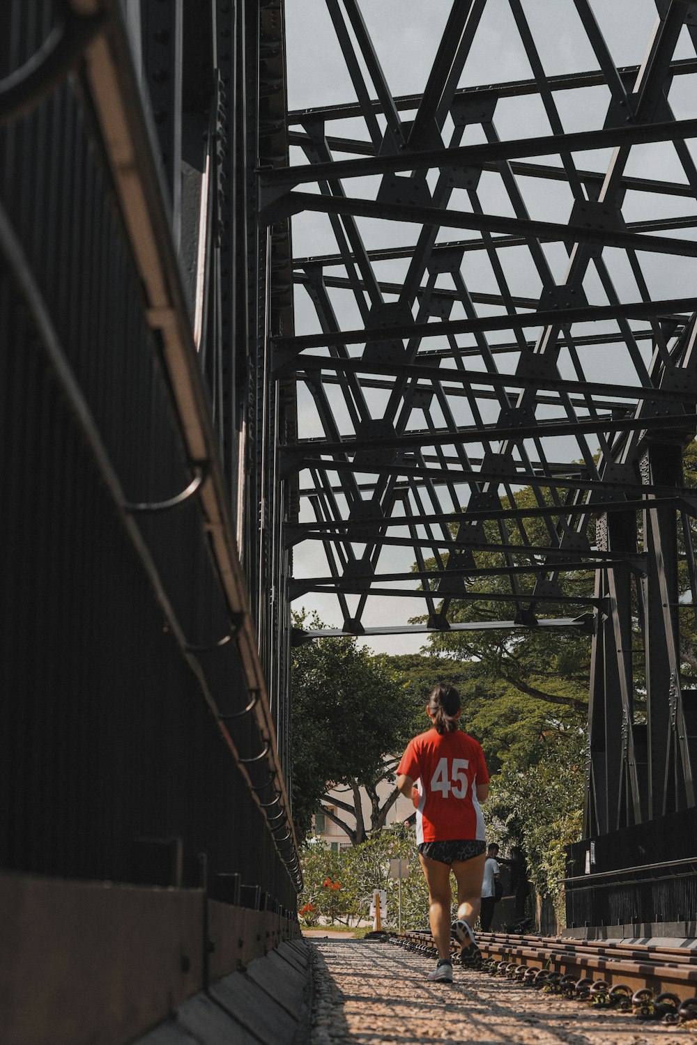 man in red t-shirt standing on brown wooden bridge during daytime