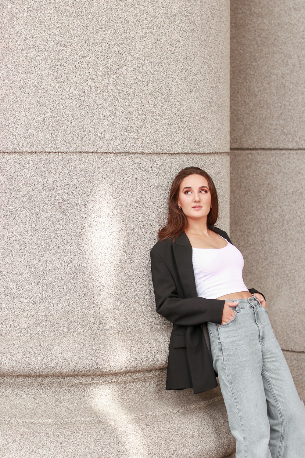 woman in black blazer and white dress standing beside grey wall