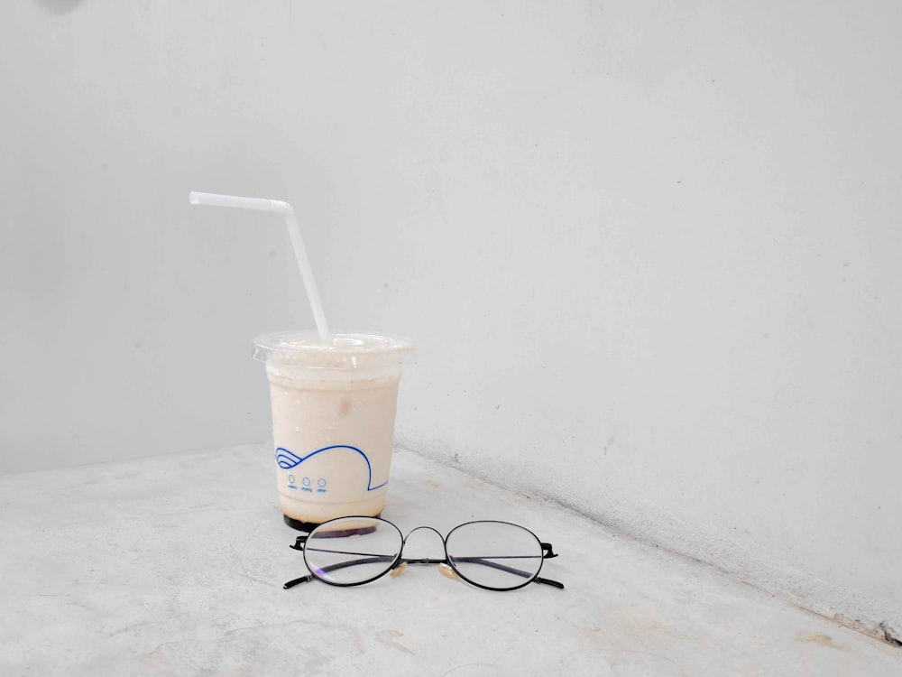 black framed eyeglasses beside white disposable cup