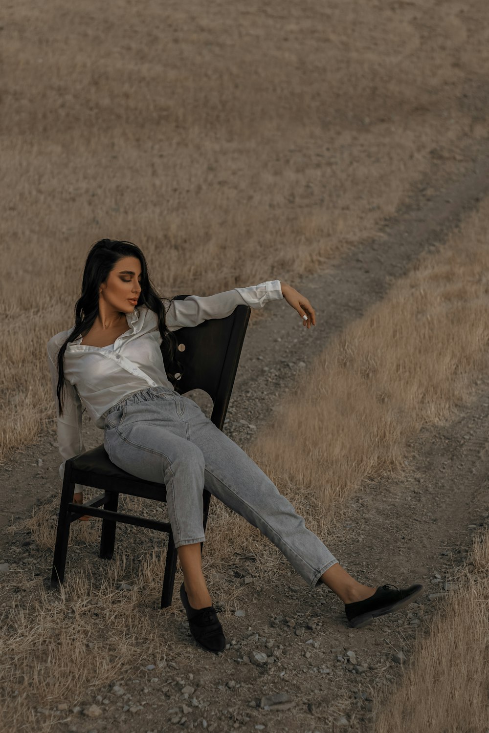 woman in white long sleeve shirt and blue denim jeans sitting on black wooden chair