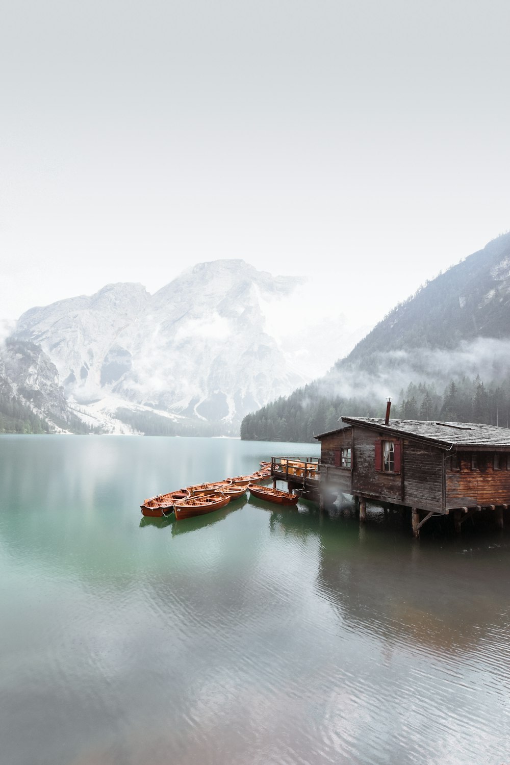 brown wooden house on lake near snow covered mountain during daytime
