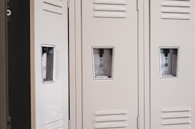 Several beige metal lockers with vented doors and rectangular handles are closely aligned.