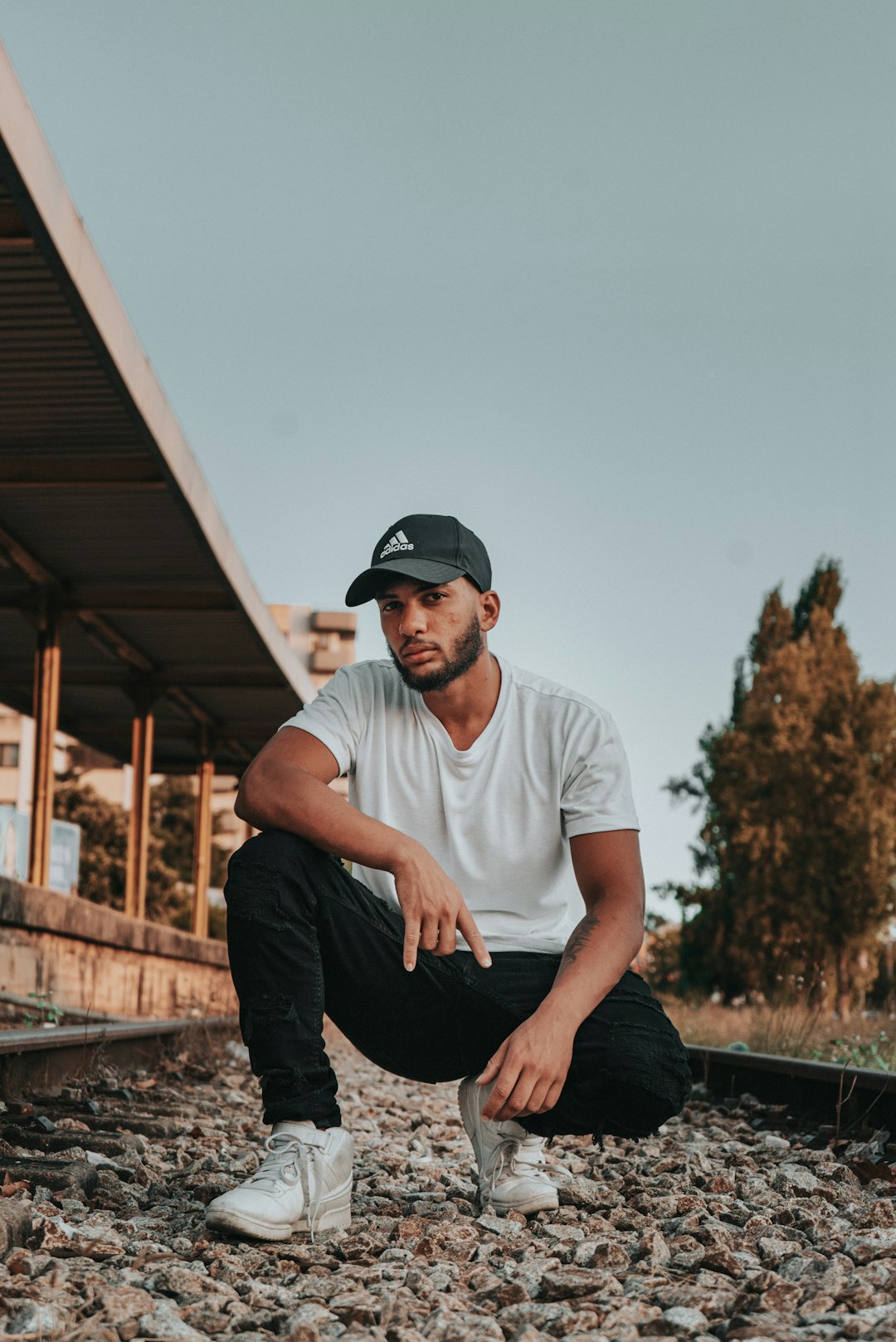 man in white crew neck t-shirt and black pants sitting on brown wooden fence during