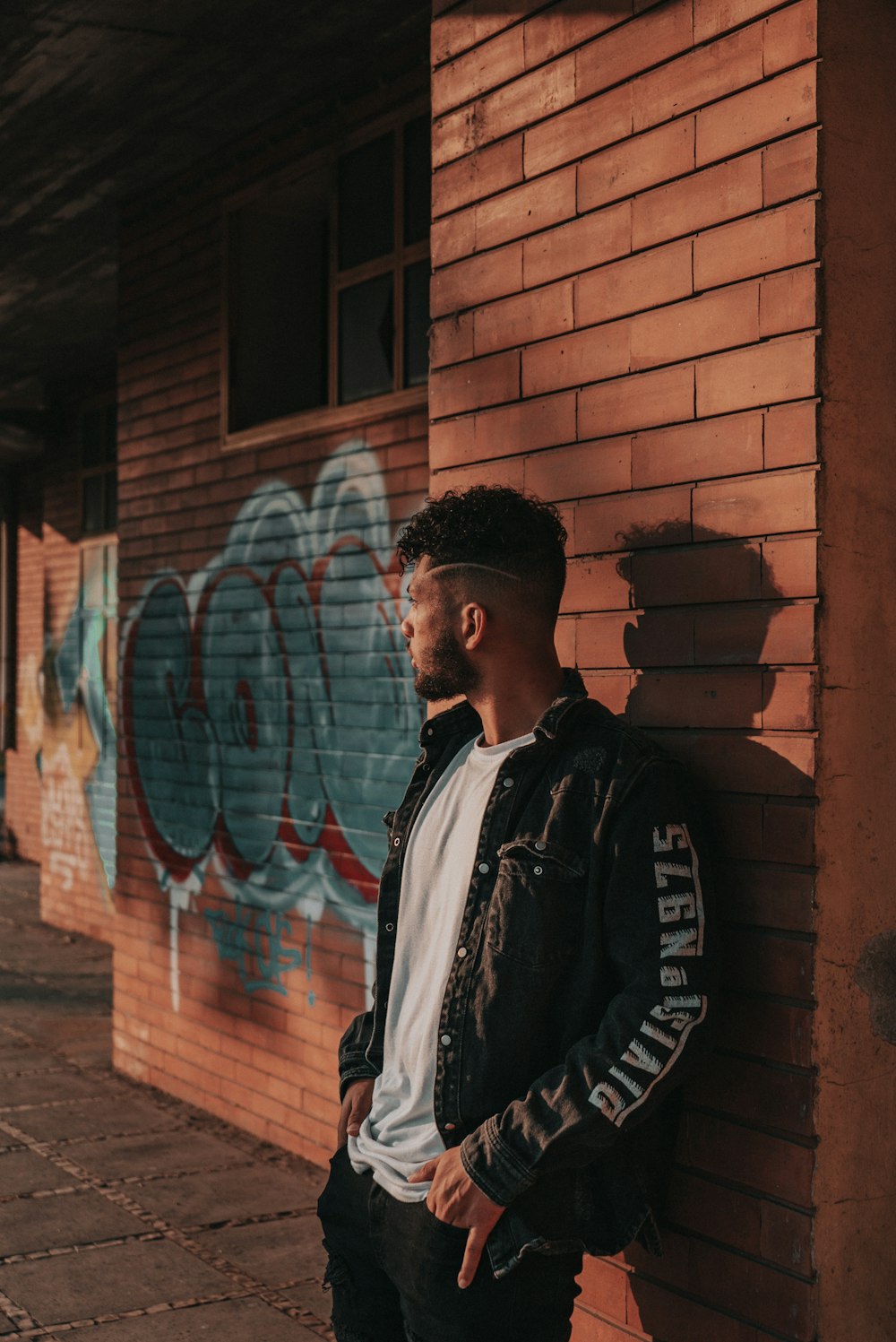 man in black and white jacket standing beside brown brick wall during daytime