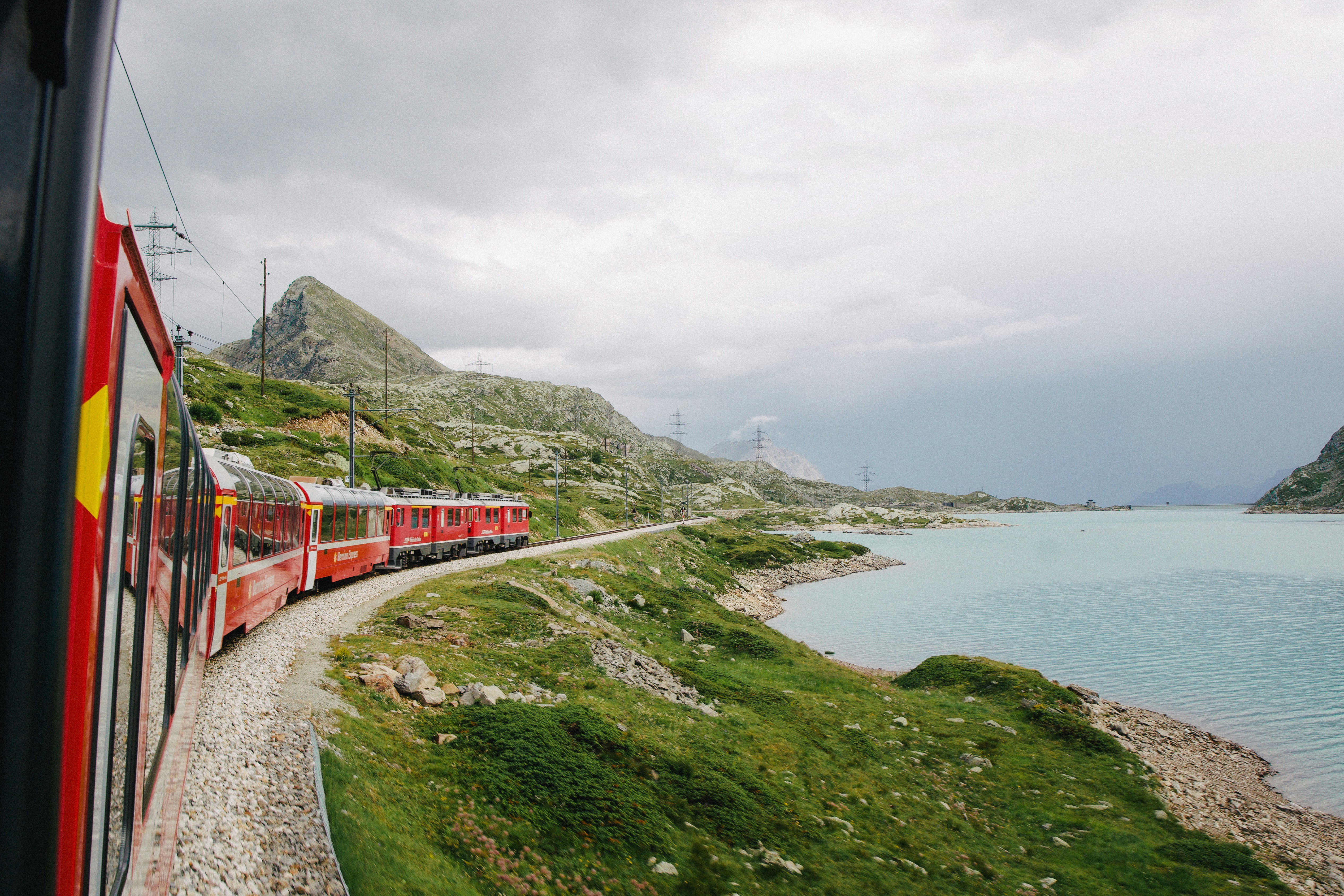 red train on rail near body of water during daytime, Bernina Express traveling and exploring the Swiss alps towards Italy, Europe