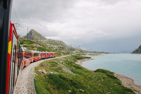 red train on rail near body of water during daytime