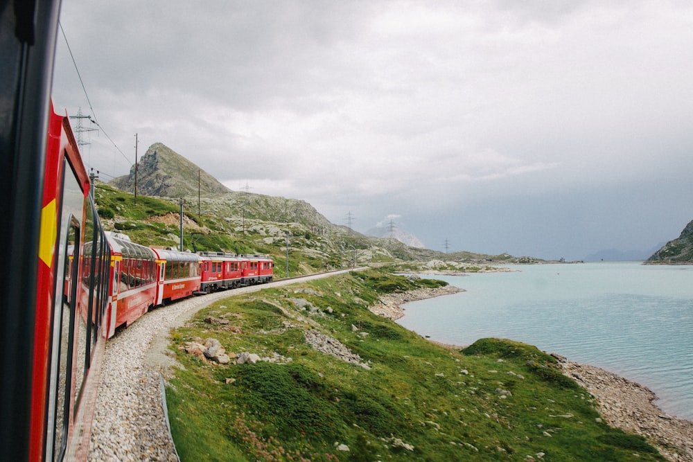 red train on rail near body of water during daytime