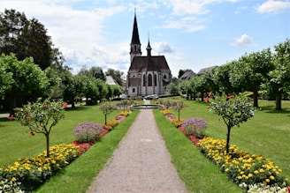 gray concrete church near green trees under white clouds during daytime