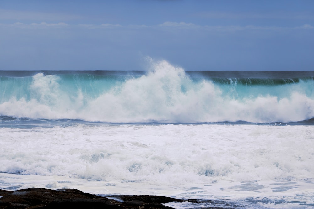 Olas oceánicas rompiendo en la formación rocosa marrón bajo nubes blancas y cielo azul durante el día