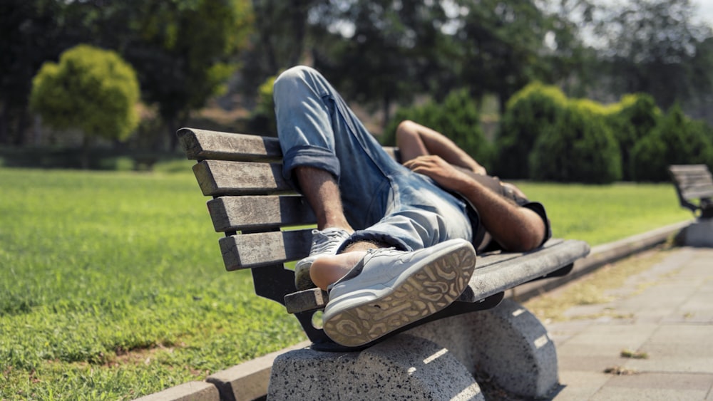 man in blue denim jeans sitting on brown wooden bench