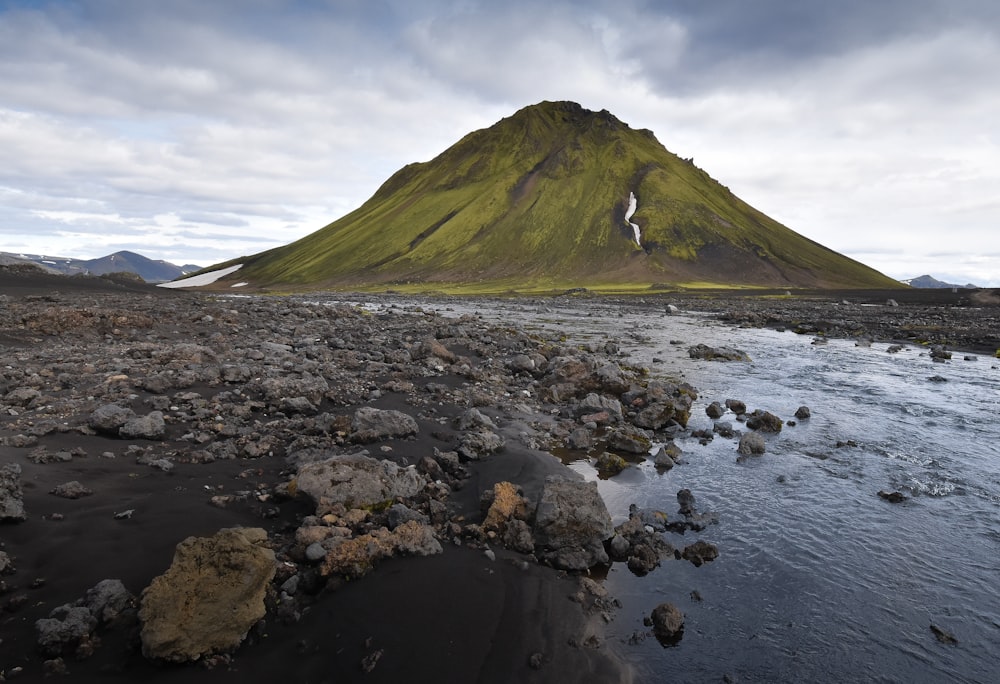 green mountain beside body of water under white clouds during daytime