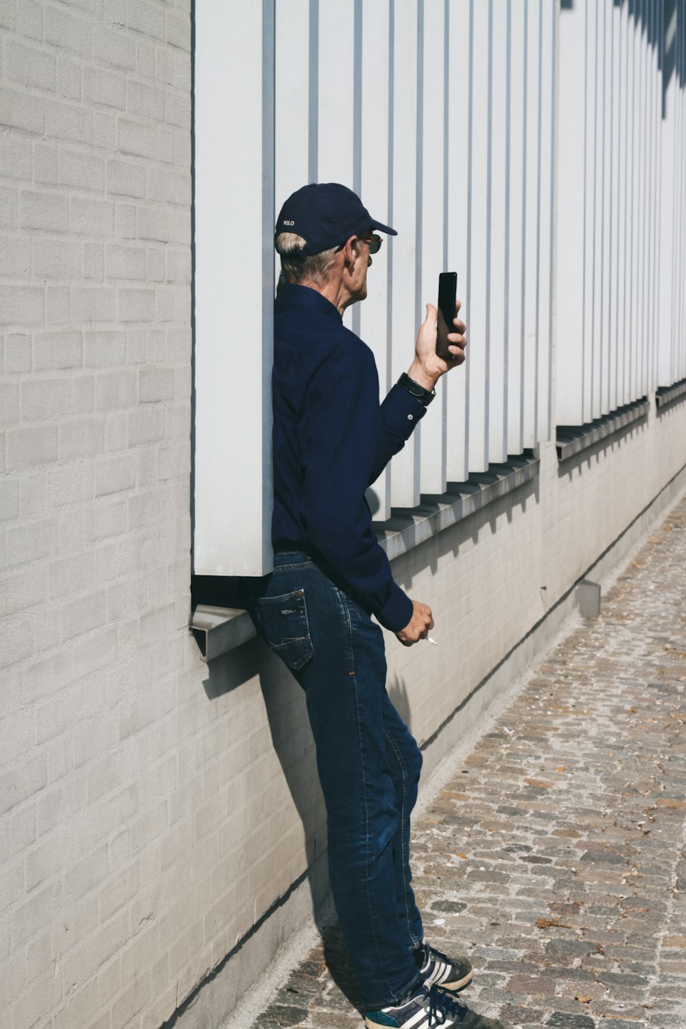Mann in schwarzem Langarmhemd und blauer Jeans mit schwarzem Smartphone