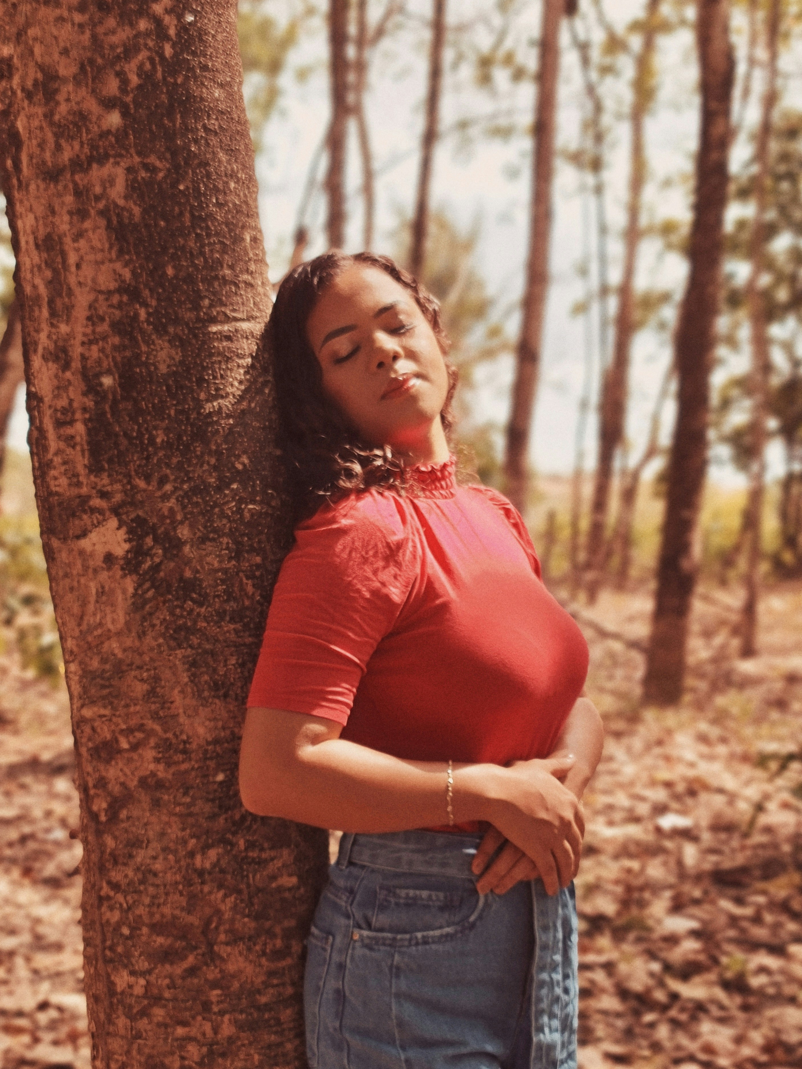赤いシャツと青いデニムのショートパンツを着た女性が茶色の木にもたれかかっている