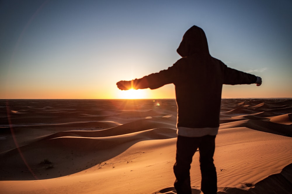 silhouette of person standing on sand during sunset