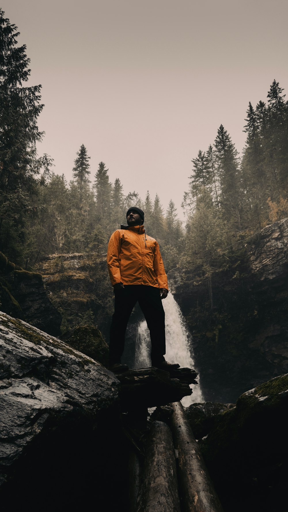 man in brown jacket standing on rock near waterfalls during daytime