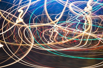 Streaks of colorful light form intricate, overlapping patterns, creating a sense of dynamic motion and energy. The lights are primarily wavy and circular, suggesting movement and chaos.