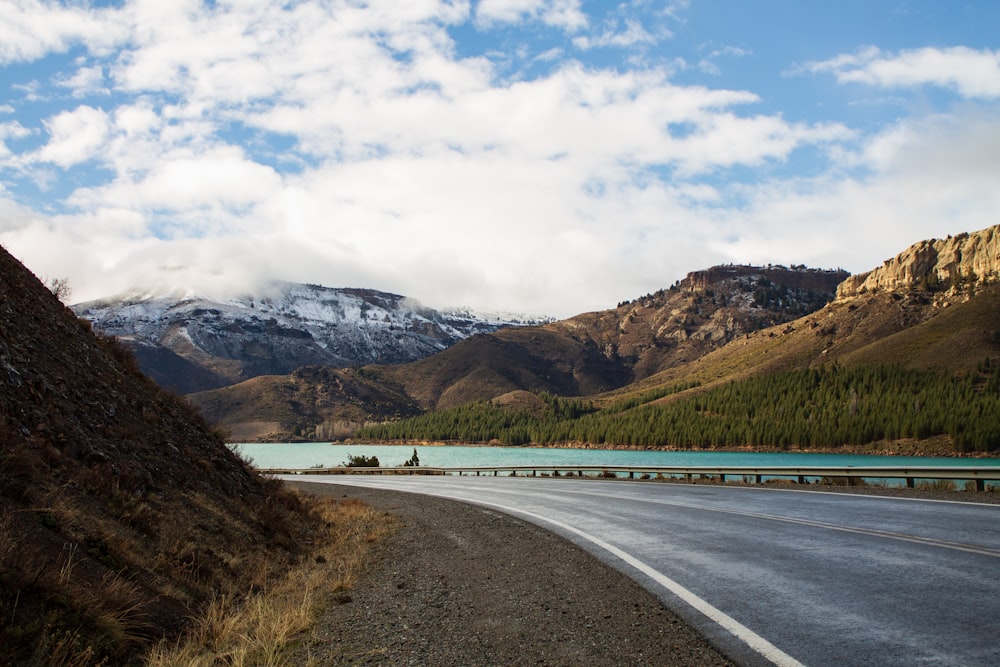 gray concrete road near brown and green mountains under white clouds during daytime