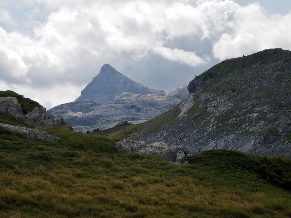 green grass field near mountain under white clouds during daytime