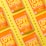 Several vibrant orange snack packages with the label 'LOVE CORN' are arranged diagonally on a bright yellow background. Each package is labeled as 'vegan cheesy flavored' and features corn kernels scattered around them.