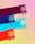 Four colorful packages of LOVE CORN, a premium crunchy corn snack, are arranged diagonally over a multicolored striped background. Each package represents a different flavor, distinguishable by their unique colors: purple, blue, teal, and red.