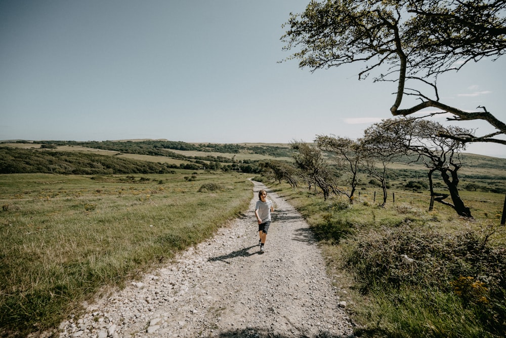 mulher na camisa branca que caminha no caminho entre o campo de grama verde durante o dia