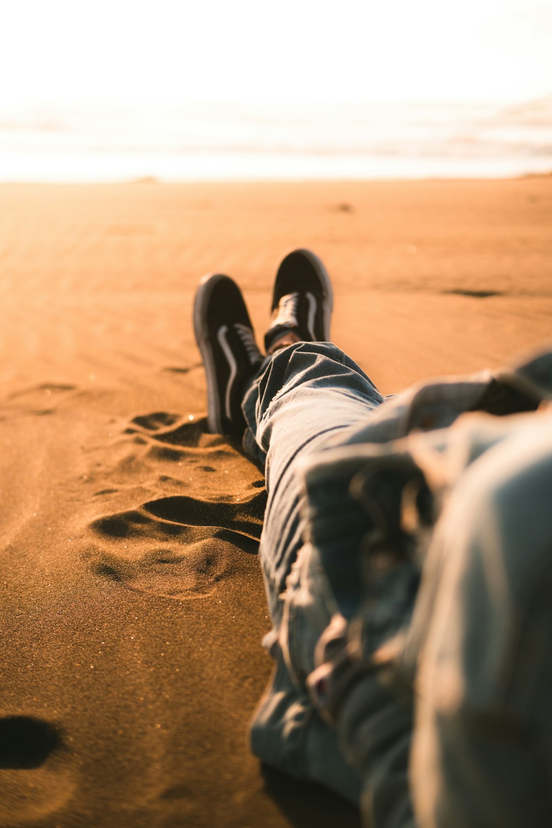 person in black and white pants and black shoes sitting on brown sand during daytime