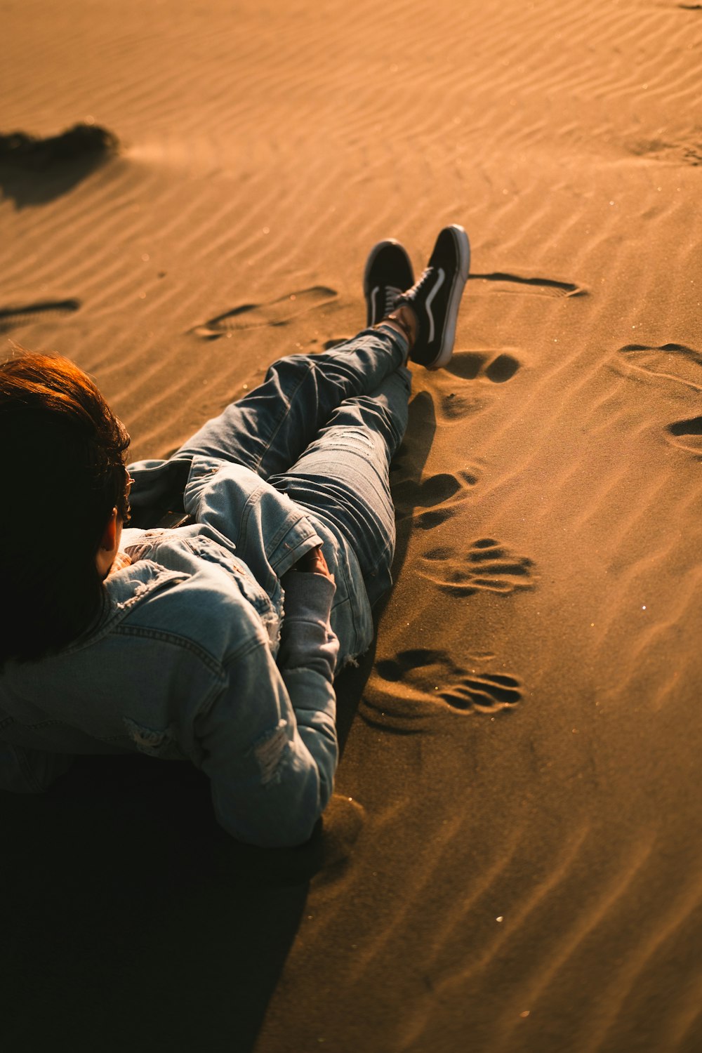 boy in blue hoodie and blue denim jeans lying on sand