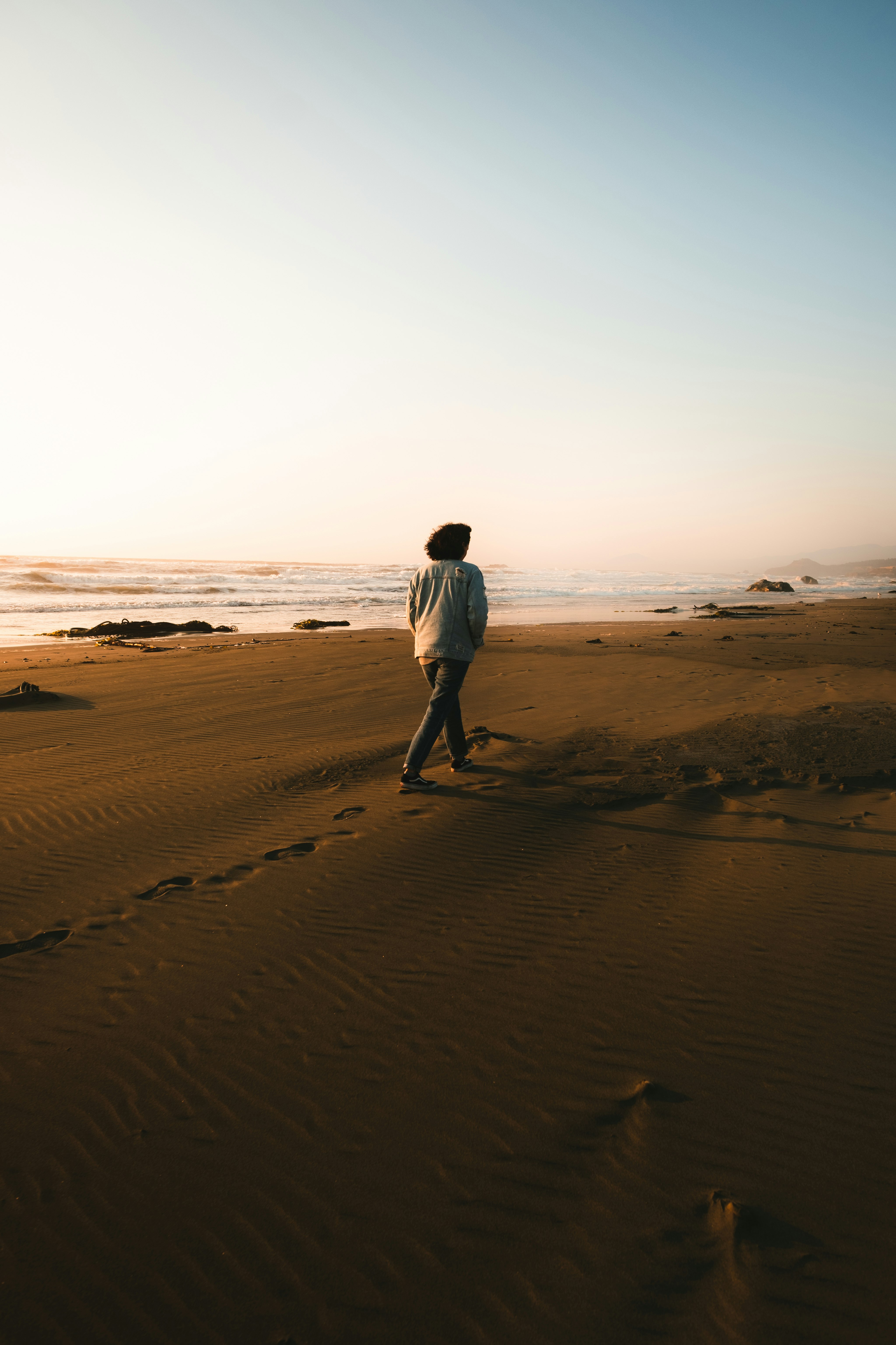 man in white shirt walking on brown sand during sunset