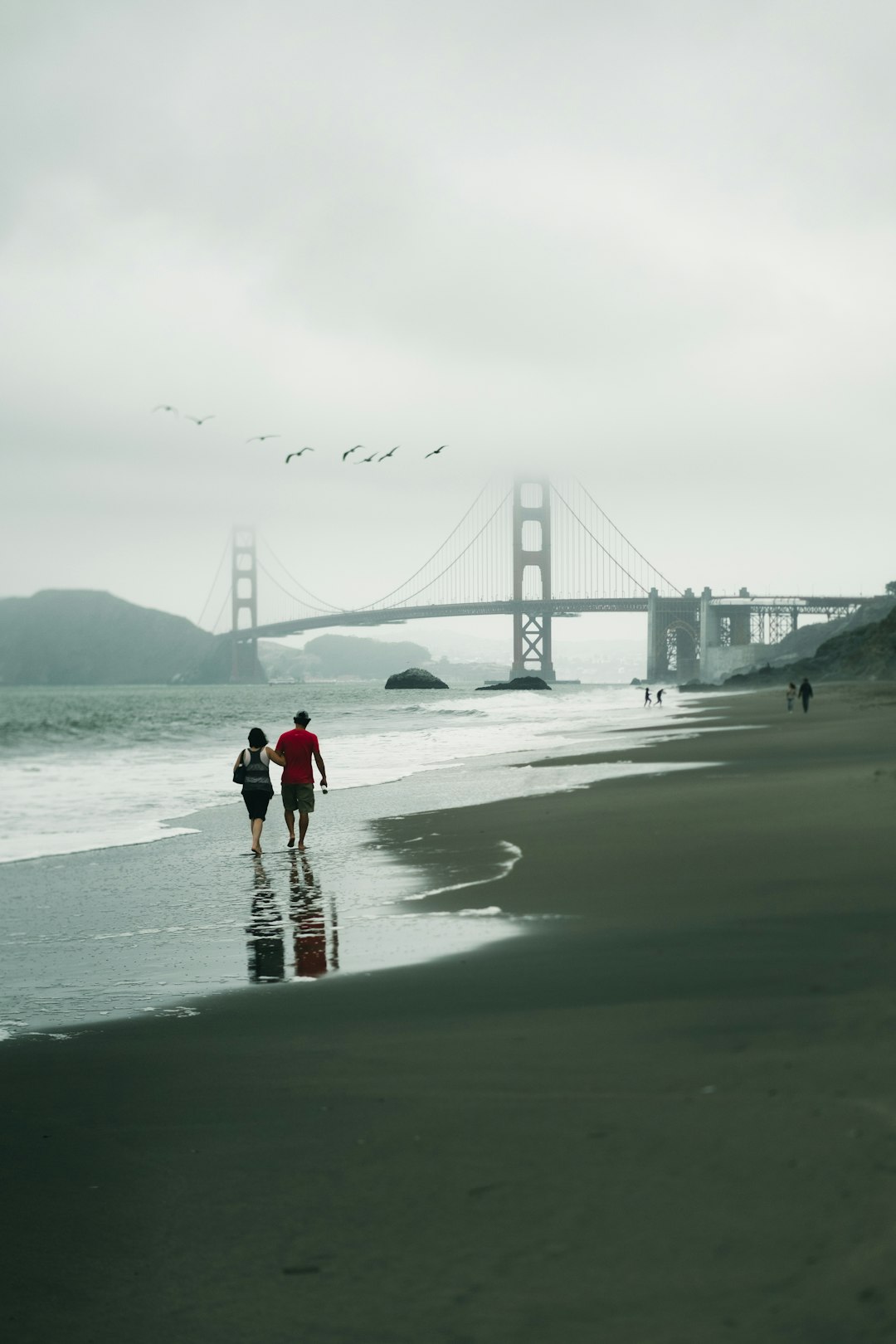 woman in red jacket and black pants walking on beach during daytime