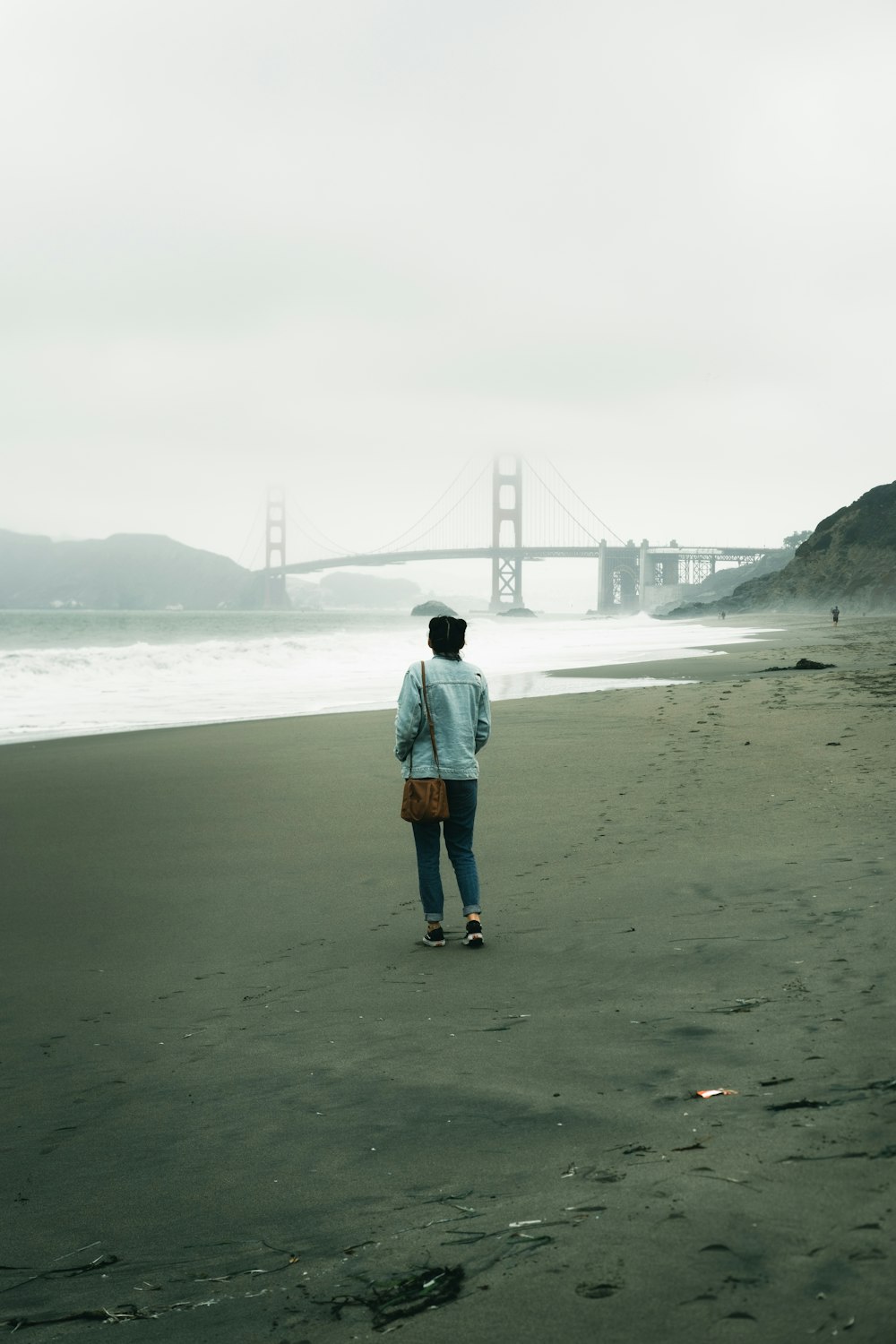 woman in blue denim jacket standing on seashore during daytime