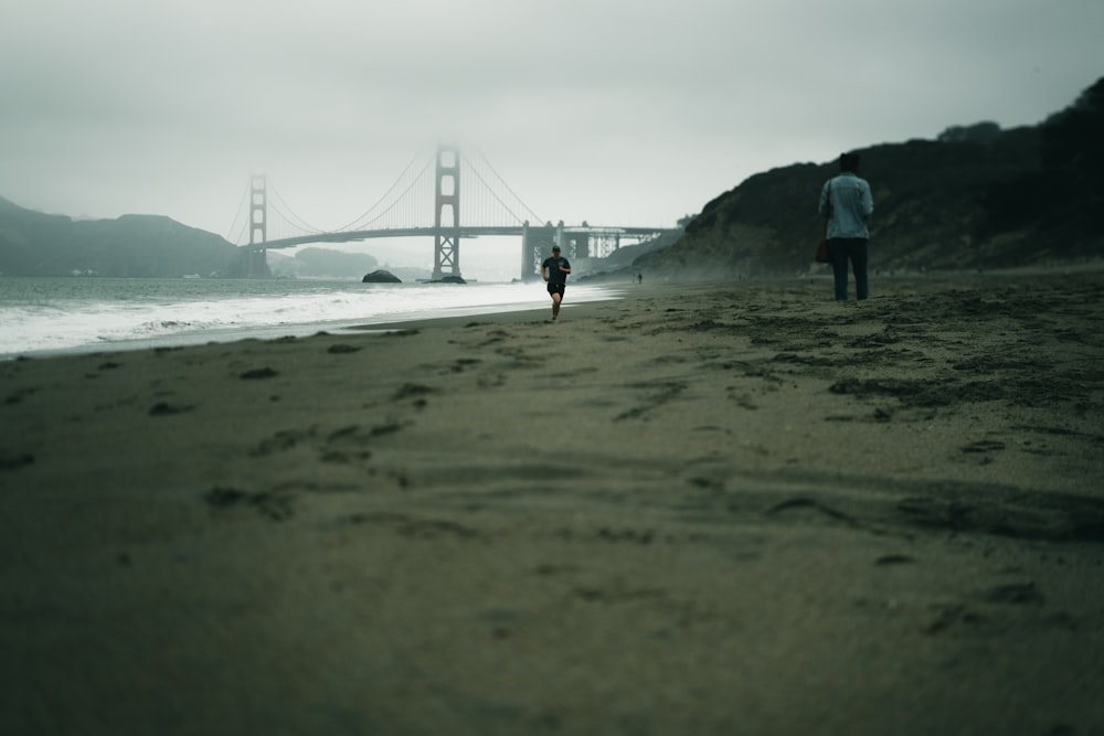 man in black jacket standing on seashore near bridge during daytime