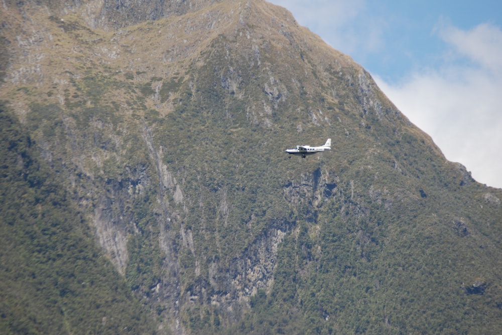 white and black airplane flying over green mountain during daytime