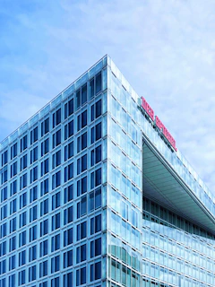 A modern glass skyscraper with a grid-like facade reflecting the sky. The building features a prominent red sign on the top reading 'DER SPIEGEL'. The clear blue sky in the background enhances the sleek and contemporary design of the structure.