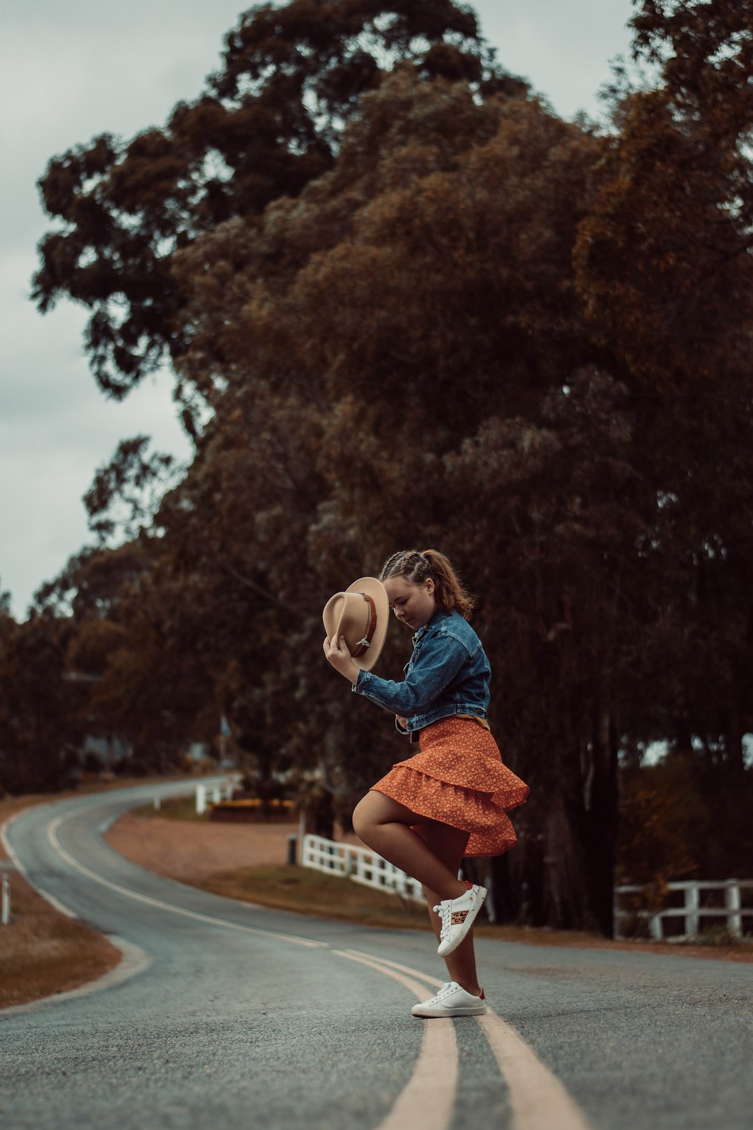 woman in blue shirt and brown skirt jumping on gray road during daytime