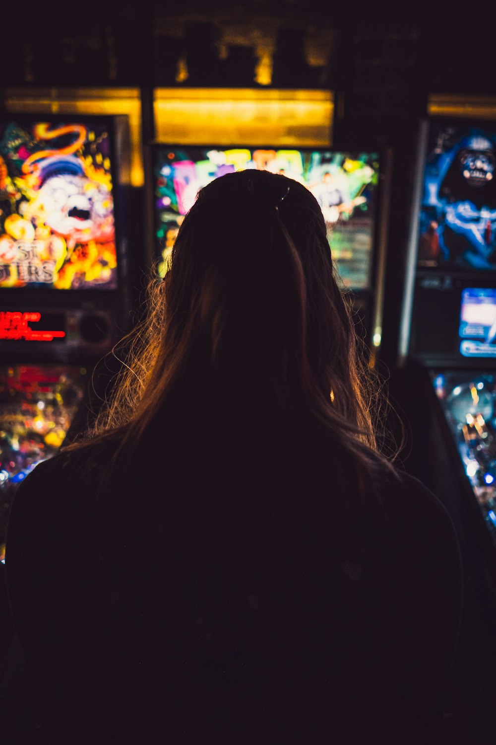 woman in black hoodie standing in front of arcade machine