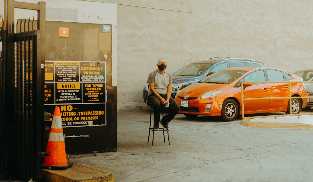 man in white dress shirt and black pants standing beside orange car during daytime