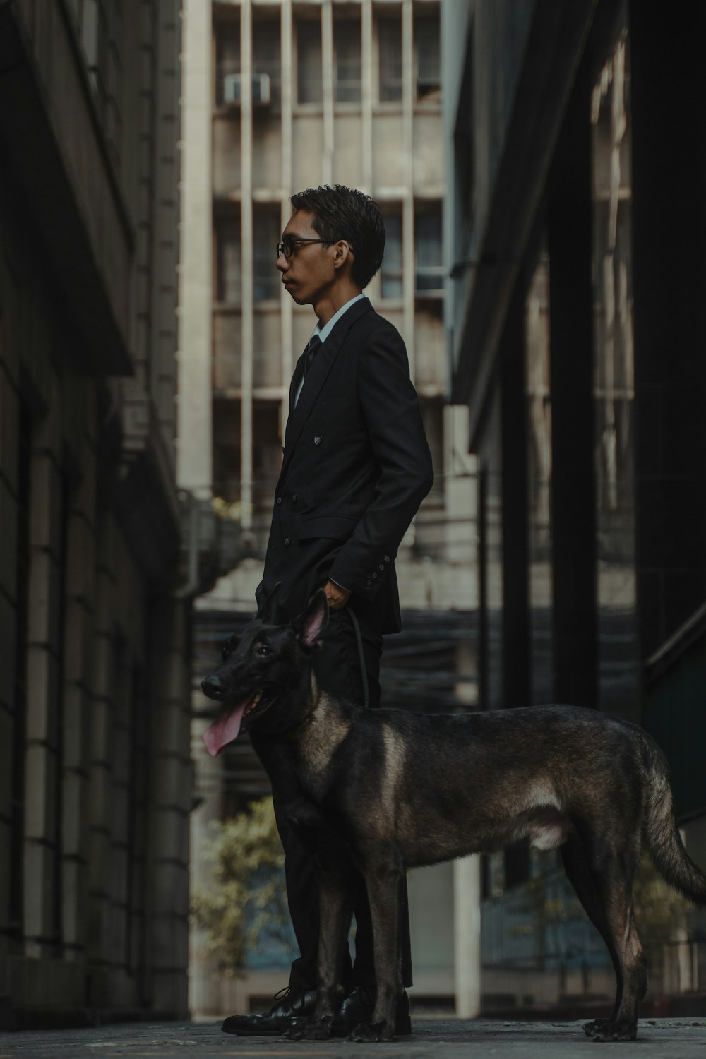 man in black jacket standing beside black short coated dog