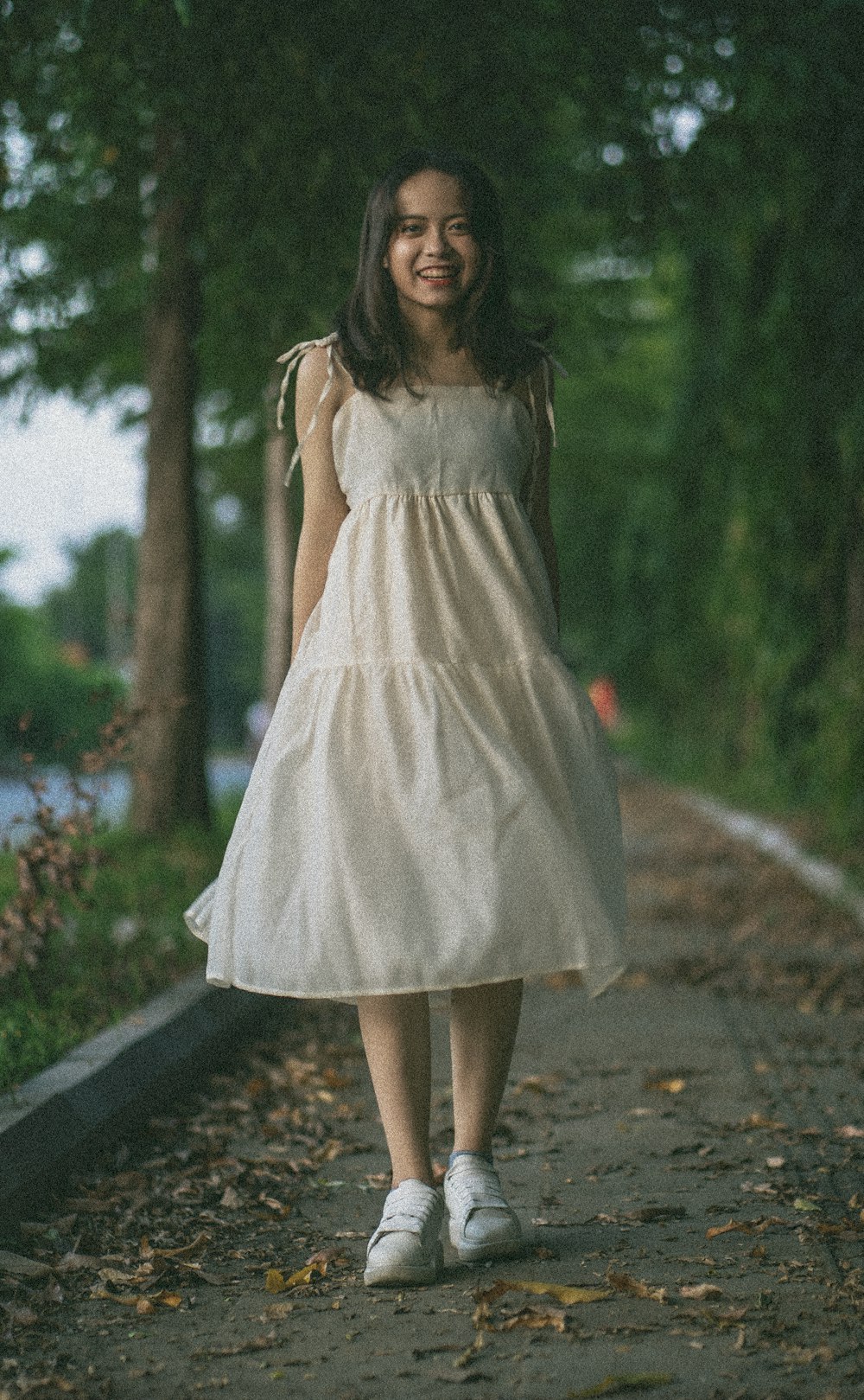 woman in white spaghetti strap dress standing on gray concrete pathway during daytime