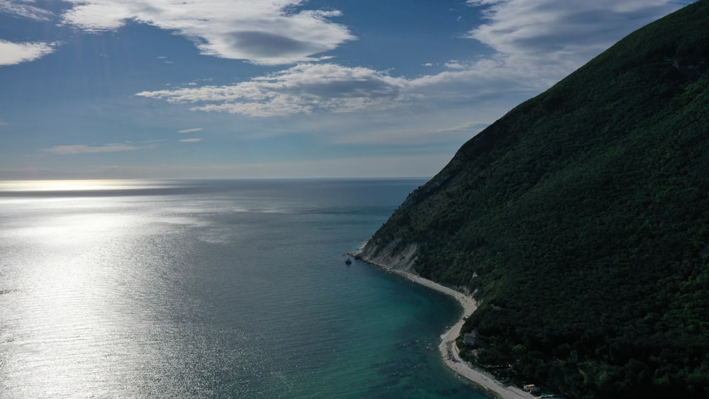 Grüner Berg neben Gewässer unter blauem Himmel tagsüber