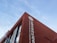A red brick building with large white lettering in both Chinese and English, featuring the words 'Shenzhen Nanshan Laixiang'. A logo appears on the top portion of the wall. The sky is clear and blue, providing a contrast to the building's vibrant color.