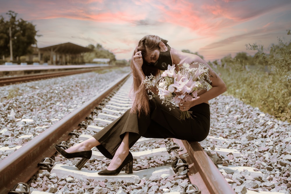 a woman sitting on a train track holding a bouquet of flowers