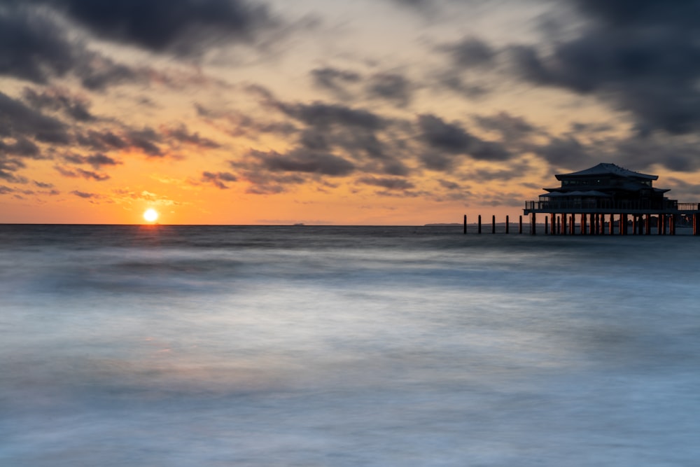 a sunset over the ocean with a pier in the distance